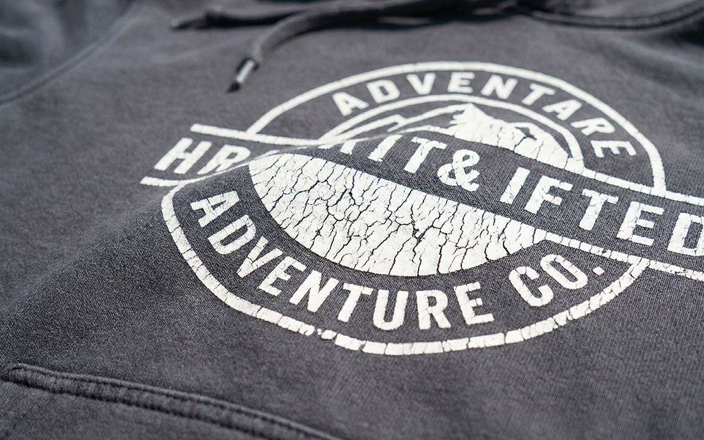 Close-up of severely cracked white print on dark hoodie showing extensive cracking throughout the design with visible flaking and peeling damage