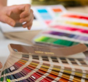 Designer holding a Pantone color guide fanned open next to printed color swatch books on a work surface