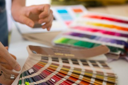 Designer holding a Pantone color guide fanned open next to printed color swatch books on a work surface