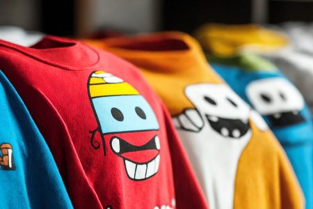 Row of colorful graphic t-shirts hanging with bright cartoon character designs showing well-maintained prints that demonstrate effective care techniques to prevent cracking