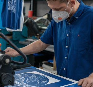 Professional screen printer operating commercial printing equipment to create durable custom designs, showing what type of t shirt printing lasts the longest through industrial screen printing processes