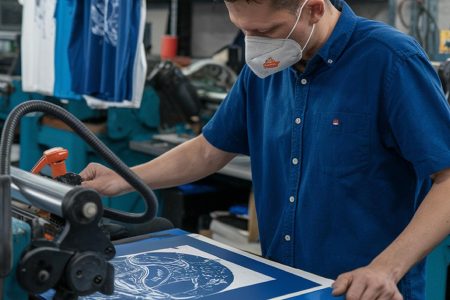Professional screen printer operating commercial printing equipment to create durable custom designs, showing what type of t shirt printing lasts the longest through industrial screen printing processes