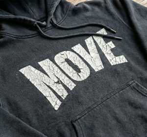 Black hoodie with severely cracked white print showing extensive cracking and peeling across printed letters on chest area